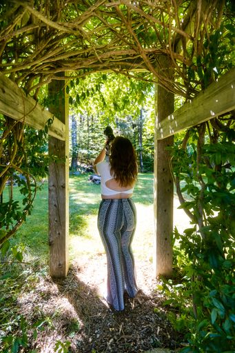A vertical image of a standing young female from the back taking a photo with a camera in a park