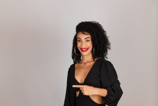 Portrait of young cheerful woman, smiling, pointing to the side. Isolated on white background in studio