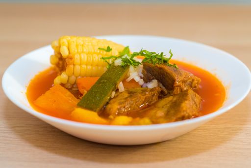 A closeup of soup in a white bowl on a wooden surface