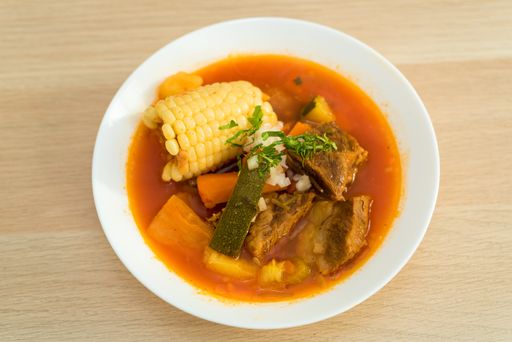 A top view of soup in a white bowl  on a wooden surface