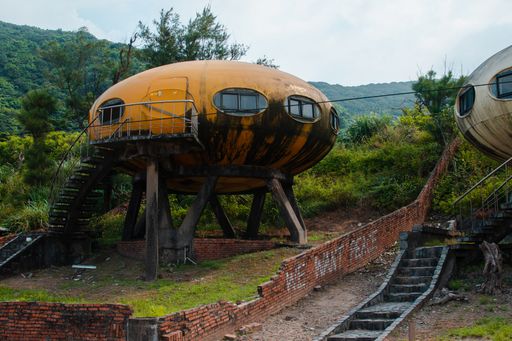 An abandoned yellow rusty UFO house near a forest in Wanli UFO Village, Taiwan