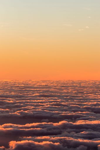 A vertical shot of the colorful and half-cloudy sunset with the view over the clouds
