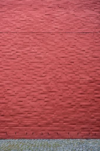 A vertical shot of a bright red painted brick wall near a road