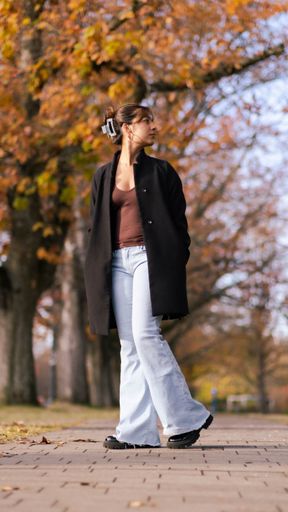 A vertical shot of a young stylish female in a black jacket posing with her hair clipped up