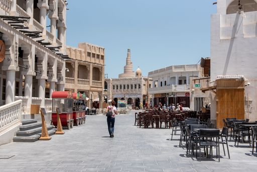 A young adult of Middle Eastern descent walking down a busy street in Doha, Qatar, during the day