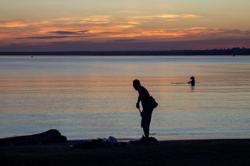 A closeup shot of a people on the coast and in the sea and cloudy sky during sunset