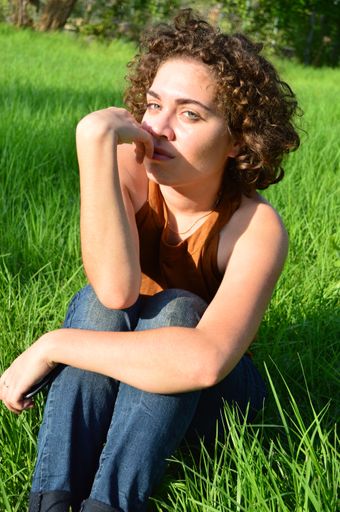 A vertical shot of a Caucasian young female with light eyes and curly hair sitting on the grass
