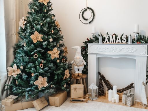 A Christmas decoration with a white fireplace, tree, candle, and brown gift boxes