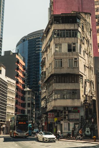 A busy Hong Kong street showcasing old and modern architecture with a bus and a white car.
