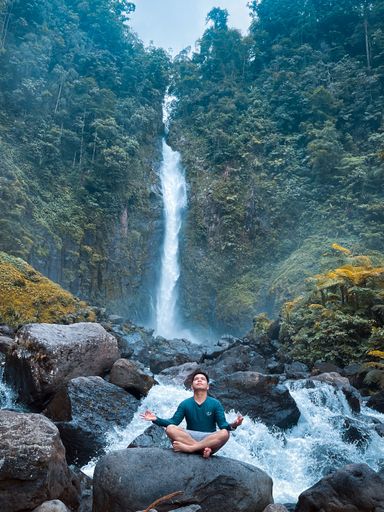 A boy in yoga pose sitting on rock near Bubuludtua Falls