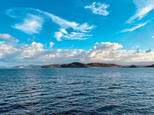 A scenic view of a blue calm sea with an island on the background under the blue sky