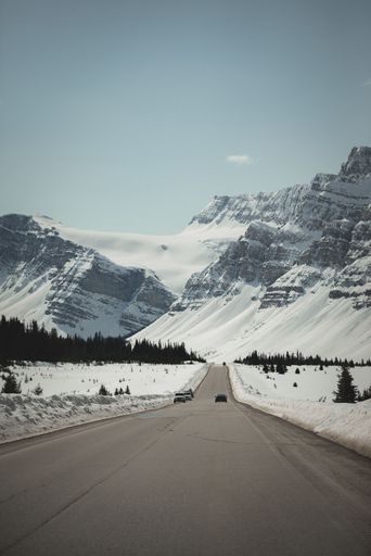 A vertical shot of long asphalt mountain road through forests leading to snowy rocky mountain