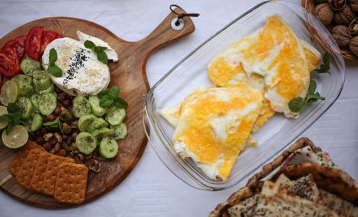 A closeup shot of a healthy breakfast with omelet, crackers, cucumber, tomatoes, lime, cheese, beans