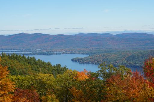 An aerial view of a lake surrounded by dense colorful forests in autumn
