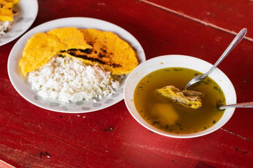 A closeup of delicious traditional Columbian dishes with beef broth, rice and arepa on a table