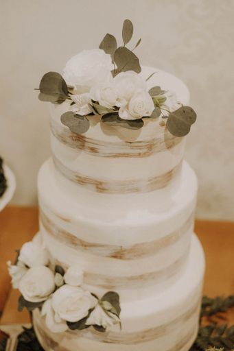 A vertical closeup shot of a layered white wedding cake with white flowers