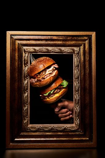 A vertical shot of a person holding two burgers on a knife through a vintage wooden frame