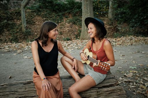 A pregnant female with her partner playing the ukulele in a park while enjoying each others' company