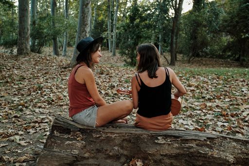 A pregnant female with her partner playing the ukulele in a park while enjoying each others' company
