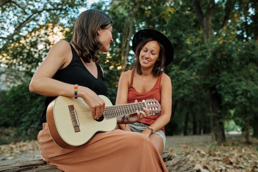 A pregnant female with her partner playing the ukulele in a park while enjoying each others' company
