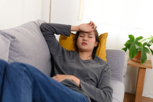 A young Asian girl suffering from headache while lying on the sofa at home and touching her head