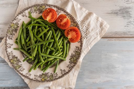 An overhead shot of fresh green beans and sliced tomatoes on a plate