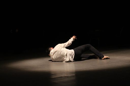 A young male laying on the floor of an illuminated stage while performing