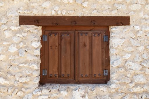 A closeup of a small wooden window of a stone building under the sunlight