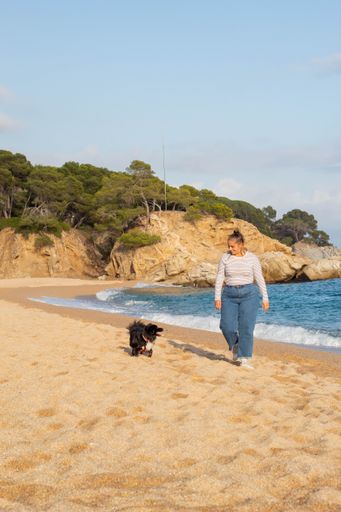 Young woman playing on the beach with her cute black dog named Loki. Running, smiling, loving and hugging each other in happy attitude and enjoying
