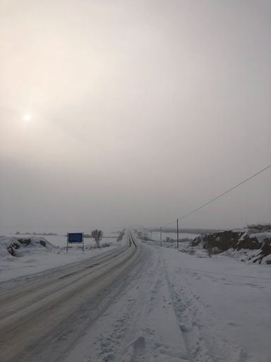 A beautiful vertical shot of highway in the center of valley covered with snow under foggy sky