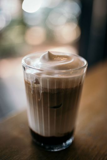 A vertical shot of a foamy coffee put on the wooden table on the blurred background