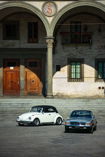 Two white and gray vintage cars in the street of Florence with old buildings