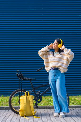 A vertical shot of a smiling young female enjoying music in her yellow headphones
