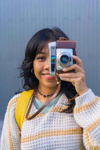 A vertical shot of a young female smiling and taking a picture with her old vintage camera