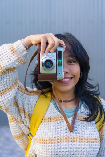 A vertical shot of a young female with a positive energy taking a photo with her vintage camera