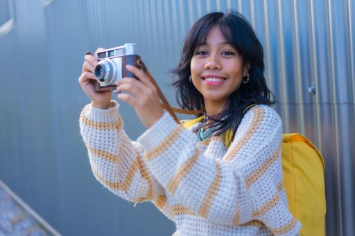 A closeup shot of a young female leaned on a metal building showing her vintage camera