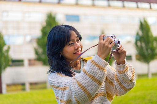 A closeup shot of a young female smiling while taking photos with her vintage camera