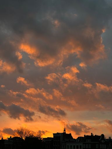 A vertical shot of sky and clouds at the sunset and the silhouette of buildings at the bottom