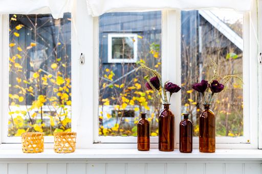 A set of brown decorative bottles serving as vases for beautiful artificial flowers set by the window