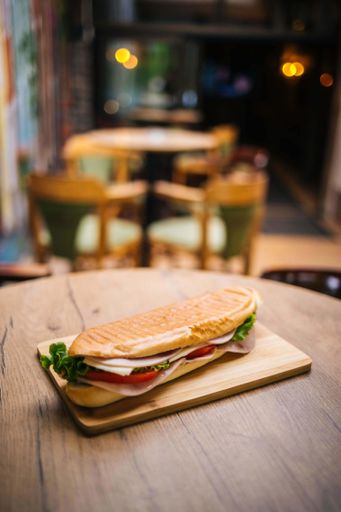 A view of a delicious looking sandwich with tomato and am on a wood board on a wooden table