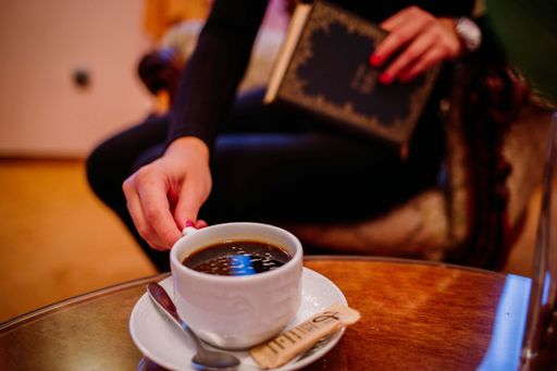 A selective focus shot of a woman drinking coffee while reading a book
