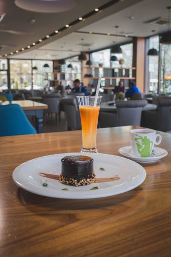 A vertical shot of a dark chocolate cake served with a cup of coffee and fresh orange juice in a cafe