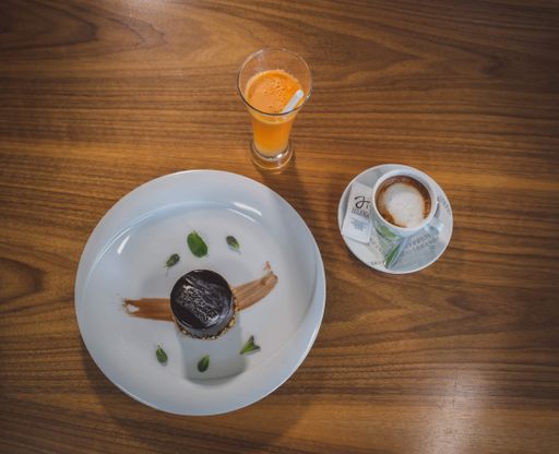 A top view of a dark chocolate cake served with a cup of coffee and fresh orange juice in a cafe