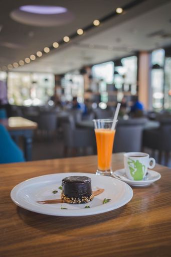 A vertical shot of a dark chocolate cake served with a cup of coffee and fresh orange juice in a cafe