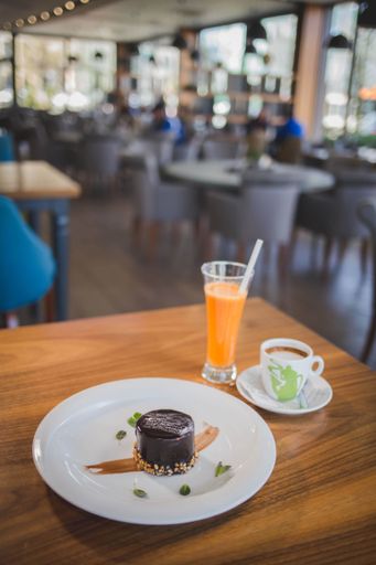A vertical shot of a dark chocolate cake served with a cup of coffee and fresh orange juice in a cafe
