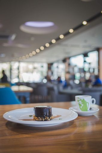A vertical shot of a dark chocolate cake served with a cup of coffee and fresh orange juice in a cafe
