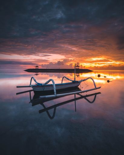 A vertical shot of a boat on the water at sunset in Pantai Karang, Sanur, Bali, Indonesia