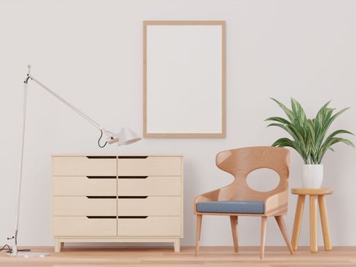 A 3d rendering of a living room with a white wall, drawer, chair, plant, and a mock-up frame.