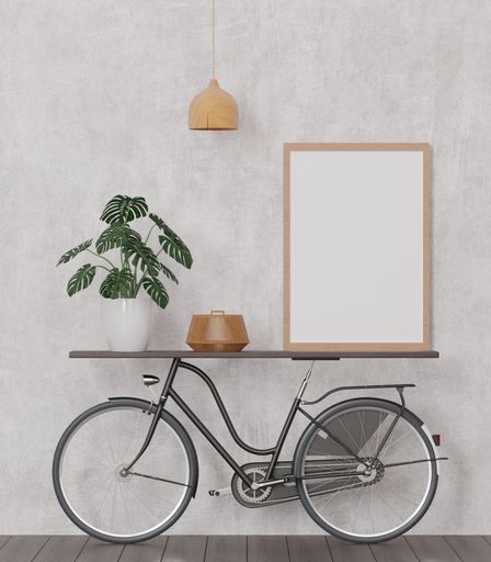A 3d rendering of a loft-style living room with a concrete wall, bicycle, mockup frame, and plant.