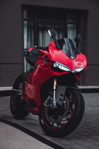 A closeup shot of a red motorcycle Ducati Panigale 1199, parked on the street, with a building in the background